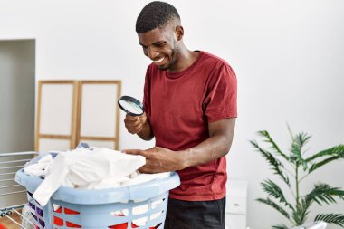 Young african american man smiling confident looking clothes using loupe at laundry room