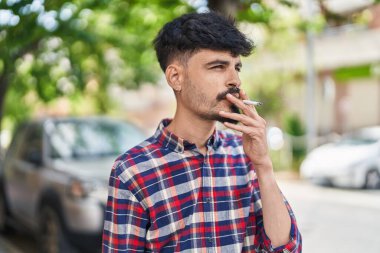 Young hispanic man smoking at street