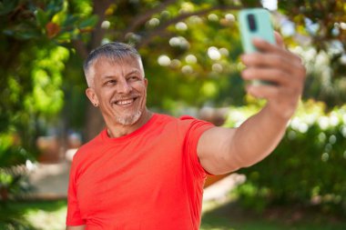 Middle age grey-haired man smiling confident making selfie by the smartphone at park