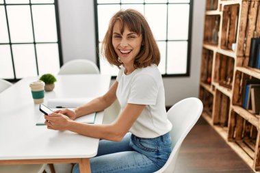 Beyaz kadın akıllı telefon kullanıyor. Evdeki masada oturuyor.