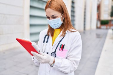 Genç beyaz kadın doktor hastanede dokunmatik ped kullanarak tıbbi maske takıyor.