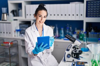 Genç beyaz kadın bilim adamı. Laboratuvarda dokunmatik ped kullanarak gülümsüyor.