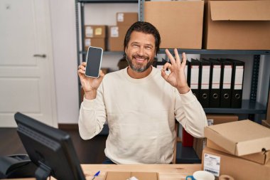 Küçük işletme şirketinde çalışan yakışıklı orta yaşlı bir adam elinde akıllı bir telefon tutuyor parmaklarıyla imza atıyor, gülümsüyor ve mükemmel bir sembol oluşturuyor. 