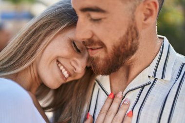 Kadın ve erkek gülümsüyor. Parkta birbirlerine sarılıyorlar.