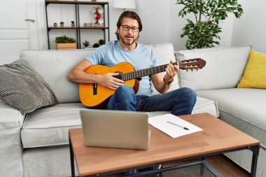 Orta yaşlı beyaz bir adam evde klasik gitar çalıyor.