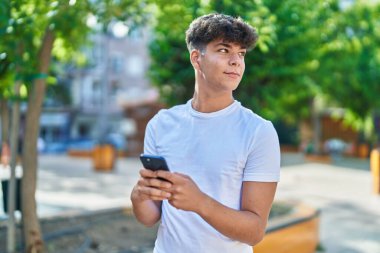 Parkta akıllı telefon kullanarak gülümseyen genç İspanyol.