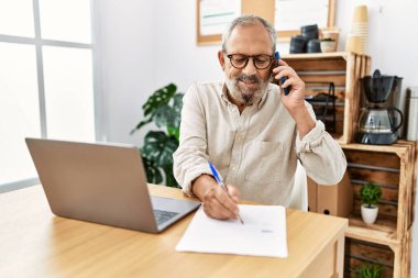 Ofiste çalışan yaşlı gri saçlı adam akıllı telefondan konuşuyor.