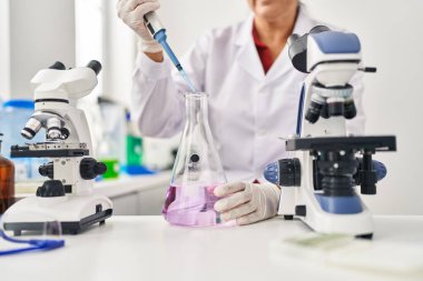 Laboratuvarda pipet kullanan orta yaşlı İspanyol kadın bilim adamı üniforması giyiyor.