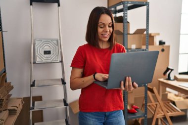 Young beautiful hispanic woman ecommerce business worker using laptop standing at office