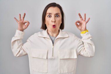 Orta yaşlı İspanyol kadın izole edilmiş arka planda duruyor. Şaşırmış ve şok olmuş görünüyor. Tamam sembolünü parmaklarıyla yapıyor. çılgın ifade 