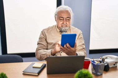 Ofiste dokunmatik ped ve dizüstü bilgisayar kullanan orta yaşlı, kır saçlı bir iş adamı.