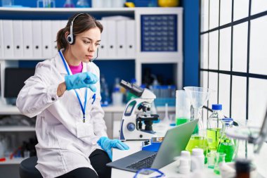 Hispanic woman working at scientist laboratory with angry face, negative sign showing dislike with thumbs down, rejection concept 