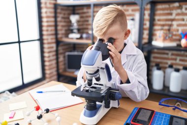Adorable toddler student using microscope standing at classroom