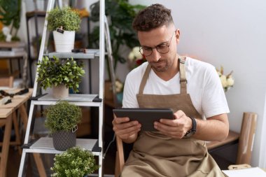 Young hispanic man florist using touchpad at flower shop