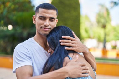 Kadın ve erkek gülümsüyor. Parkta birbirlerine sarılıyorlar.