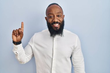 African american man standing over blue background showing and pointing up with finger number one while smiling confident and happy. 