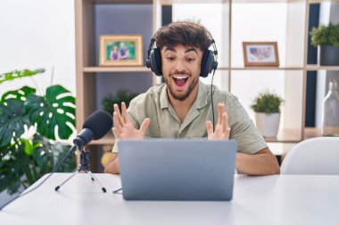 Arab man with beard working at the radio celebrating victory with happy smile and winner expression with raised hands 