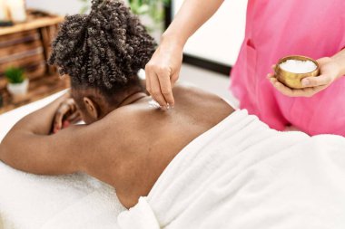 Afro-Amerikalı kadın güzellik salonunda tuz kullanarak sırt masajı yaptırıyor.