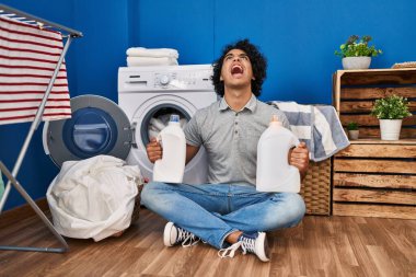 Kıvırcık saçlı İspanyol bir adam çamaşır deterjanı tutuyor kızgın ve öfkeli çığlıklar atıyor öfkeyle bağırıyor öfkeyle yukarı bakıyor. 