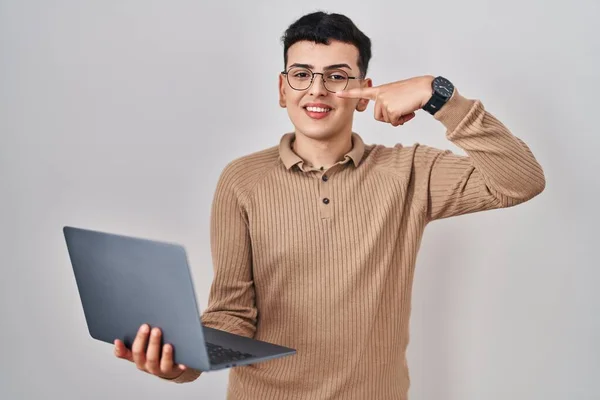 Non binary person using computer laptop pointing with hand finger to face and nose, smiling cheerful. beauty concept