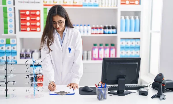 Young Hispanic Girl Pharmacist Writing Report Clipboard Pharmacy — Foto de Stock
