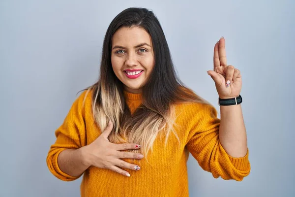 Young hispanic woman standing over isolated background smiling swearing with hand on chest and fingers up, making a loyalty promise oath