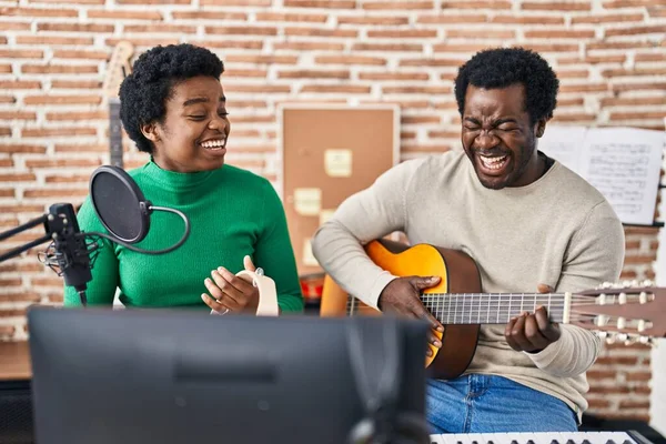 African american man and woman music group singing song playing guitar and tambourine at music studio