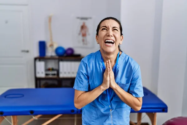 Mladá Hispánka Uniformě Fyzioterapeutky Stojí Klinice Prosí Modlí Rukama Sepjatýma — Stock fotografie