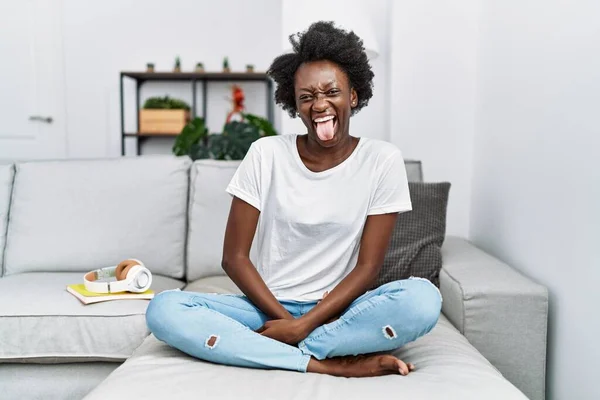Afrykańska Młoda Kobieta Siedząca Kanapie Domu Wystająca Języka Szczęśliwa Śmiesznym — Zdjęcie stockowe