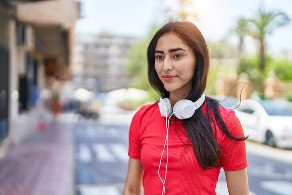年轻的惊慌失措的女孩带着耳机自信地微笑在街上 — 图库照片