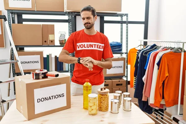 Young Hispanic Man Wearing Volunteer Shirt Donations Stand Checking Time — Stock Photo, Image