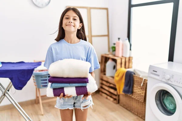 Young hispanic girl holding folded laundry smiling with a happy and cool smile on face. showing teeth.