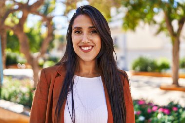 Genç İspanyol kadın parkta yürürken kendinden emin gülümsüyor.