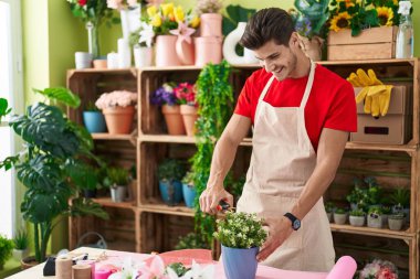Young hispanic man florist cutting plants at flower shop