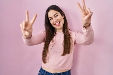 Pembe arka planda dikilen esmer kadın iki elini de göstererek gülümseyerek zafer işareti yapıyor. İki numara.. 
