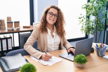 Genç, güzel İspanyol iş kadını. Ofisteki evraklarda dizüstü bilgisayar kullanıyor.