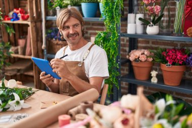 Young blond man florist smiling confident using touchpad at flower shop