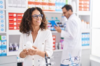 Erkek ve kadın eczacılar dokunmatik ped kullanıyorlar ve eczanede ilaç şişesi tutuyorlar.