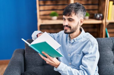 Evdeki kanepede oturmuş kitap okuyan genç bir İspanyol.