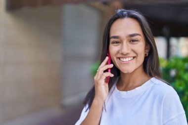 Genç, güzel, İspanyol bir kadın gülümsüyor ve caddede akıllı telefondan konuşuyor.