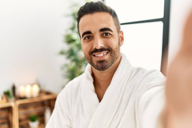 Bornoz giyen genç İspanyol adam güzellik merkezinde fotoğraf çekiyor.