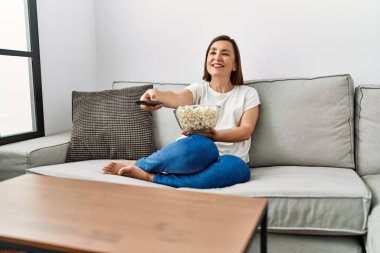 Orta yaşlı İspanyol kadın evde patlamış mısır yiyerek film izliyor.