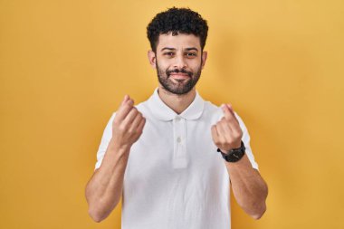 Sarı arka planda duran Arap adam elleriyle para hareketi yapıyor, maaş istiyor, milyonerlik işi yapıyor. 