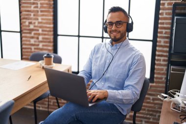 Young hispanic man business worker using laptop and headphones at office