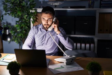 Genç İspanyol iş adamı telefonda konuşuyor, ofiste fazla mesai yapıyor.