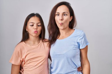Young mother and daughter standing over white background making fish face with lips, crazy and comical gesture. funny expression. 