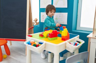 Adorable toddler playing with construction blocks standing at kindergarten