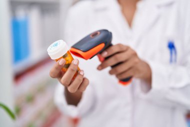 Genç ve güzel İspanyol kadın eczacı eczanede ilaç şişesini tarıyor.