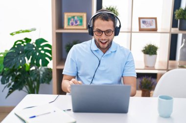 Bilgisayar bilgisayarı kullanan, kulaklık takan, ağzı açık, korkmuş ve şaşırmış İspanyol bir adam. 