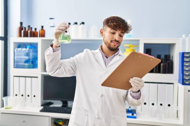 Young arab man scientist measuring liquid reading report at laboratory